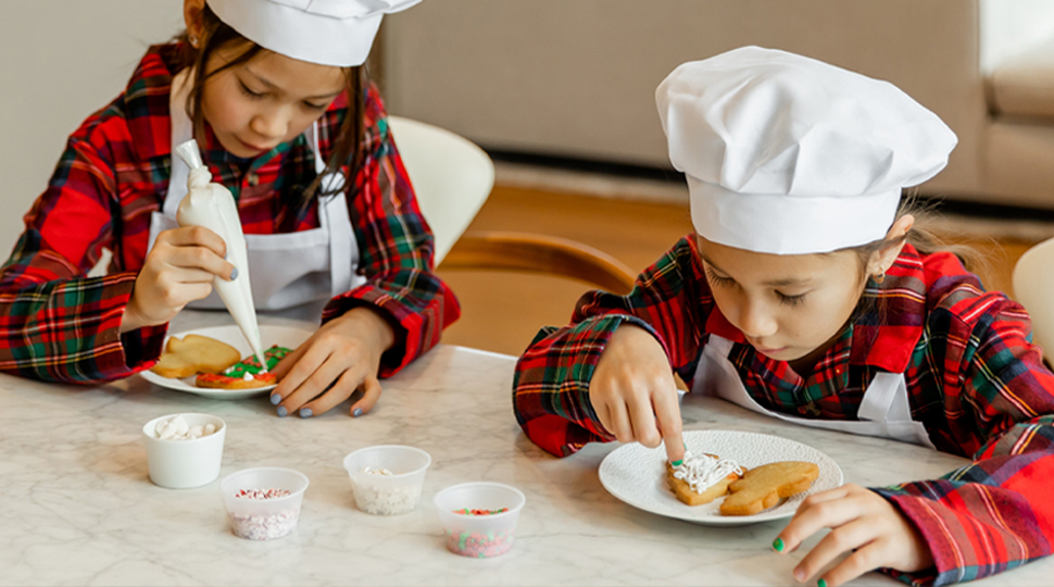 Two children wearing chef hats and decorating cookies.