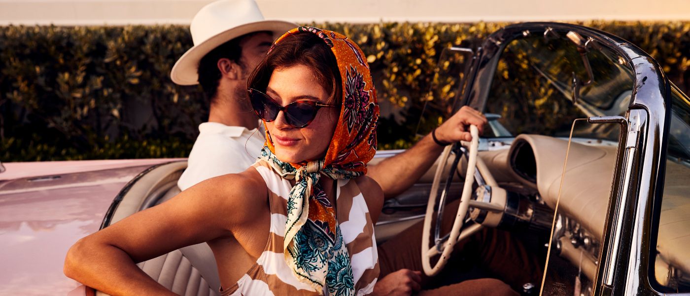 A woman in a scarf and a man in a hat in an old vintage car
