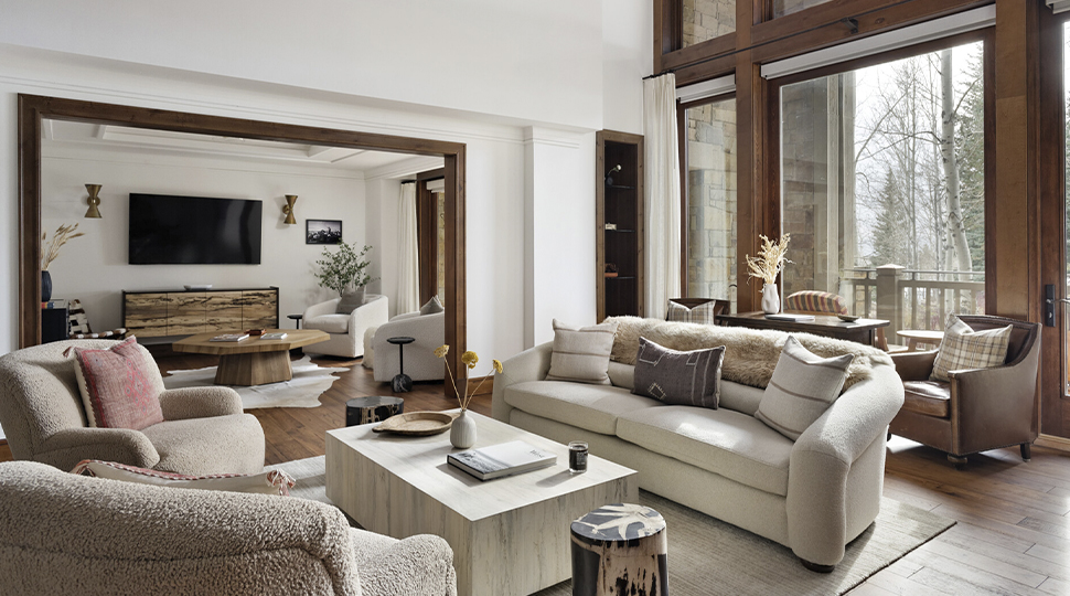 A modern living area with plush couches and chairs, multiple seating areas and large windows overlooking a snowy forest