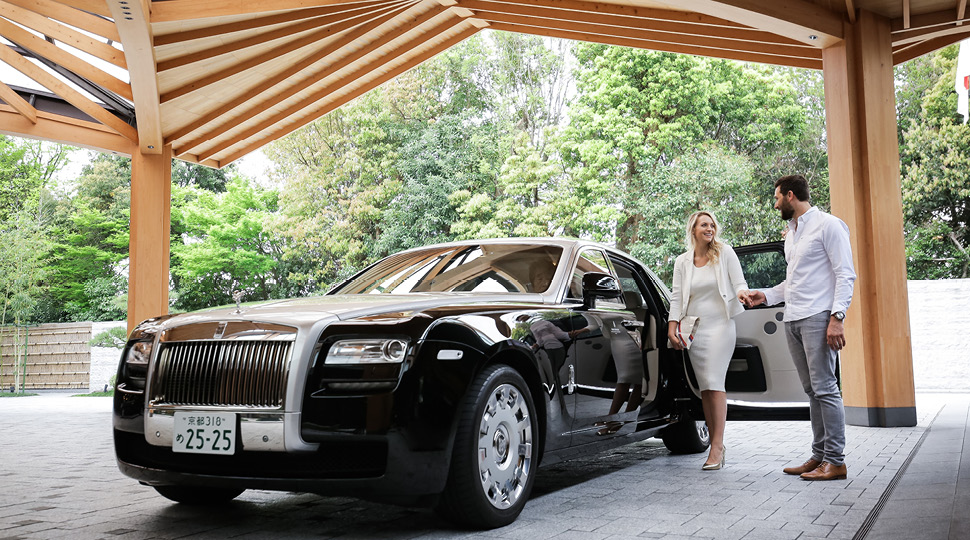 A woman in a white dress and a man in a white button-up shirt step out of a Rolls Royce