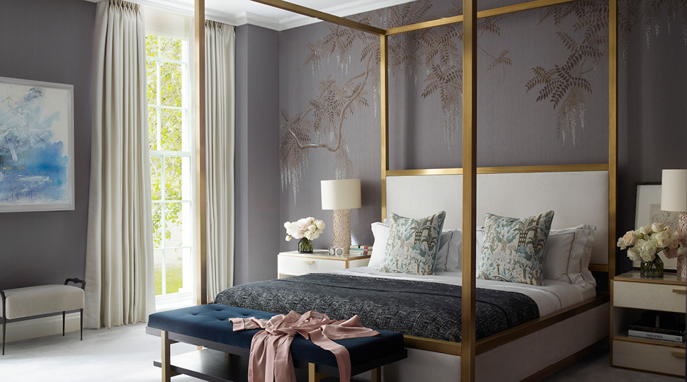 A king bed with a gold frame and printed tropical pillows with a pink robe draped on a teal ottoman at the foot of the bed