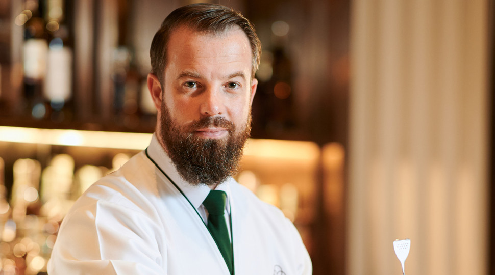 Philip Bischoff, Beverage Manager, BKK Social Club, Four Seasons Hotel Bangkok at Chao Phraya River and Beverage Ambassador, Four Seasons Asia Pacific, poses in front of a modern bar