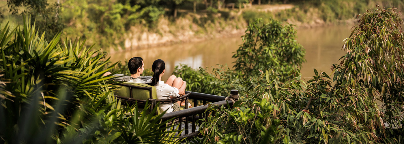 A couple sits on an outdoor couch overlooking the jungle