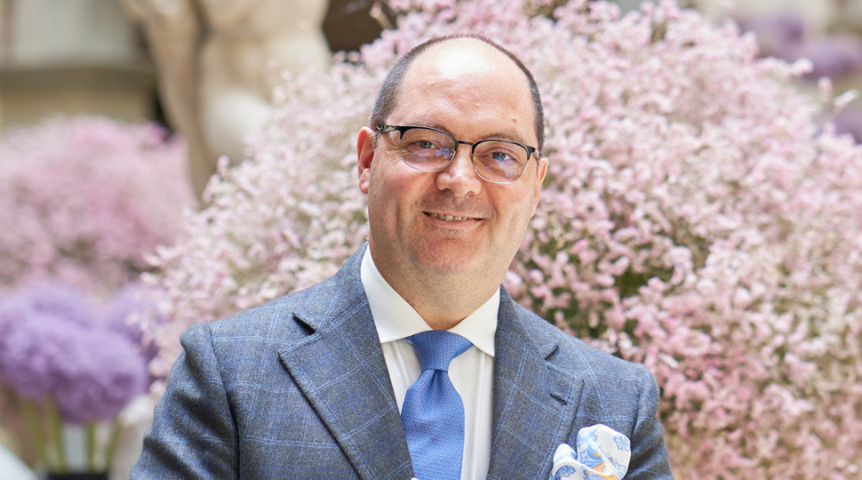 Max Musto, General Manager at Four Seasons Hotel Firenze, smiles in front of pink and purple floral arrangements