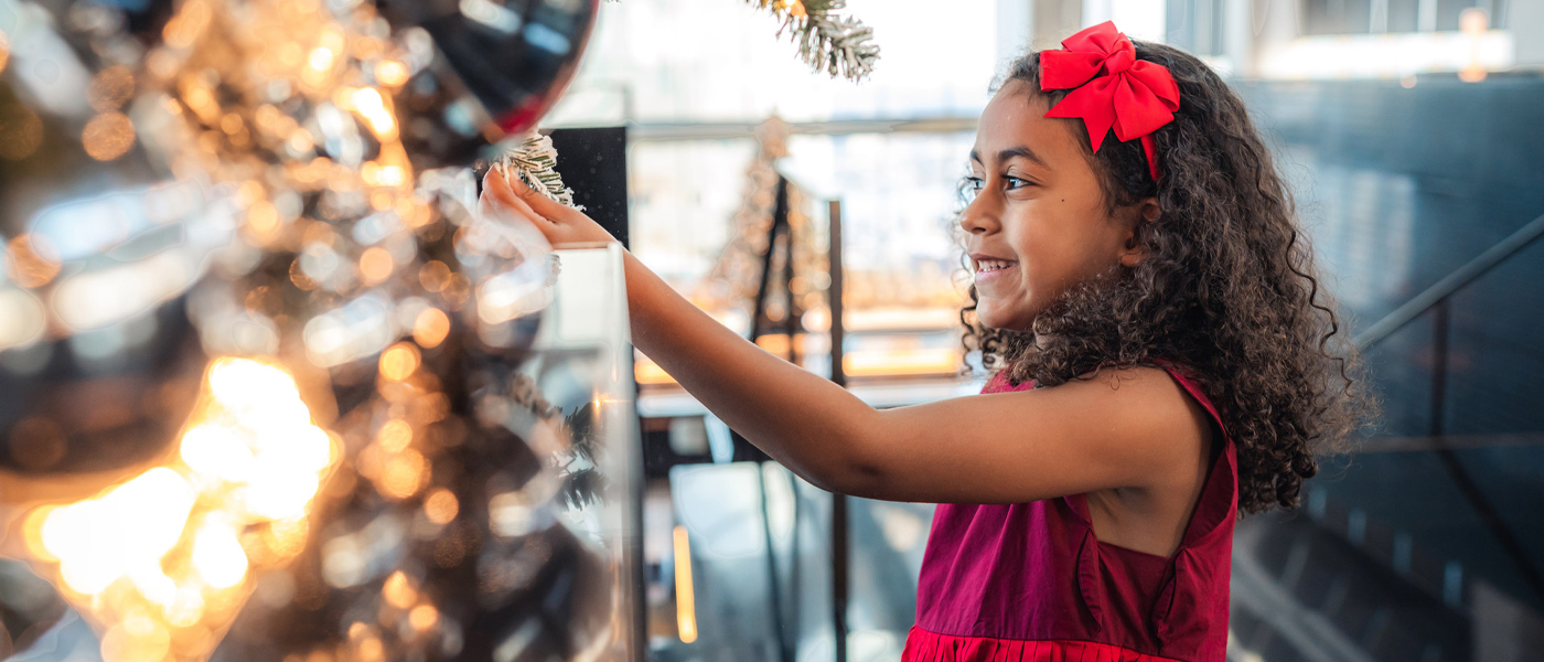 A young girl in a red dress touches the branch of a festive tree