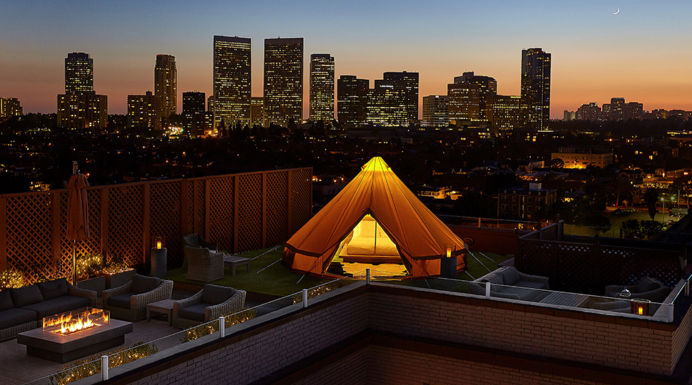 Glowing white tent, bed on rooftop patio by chairs, outdoor fireplace, Beverly Hills sunset city views