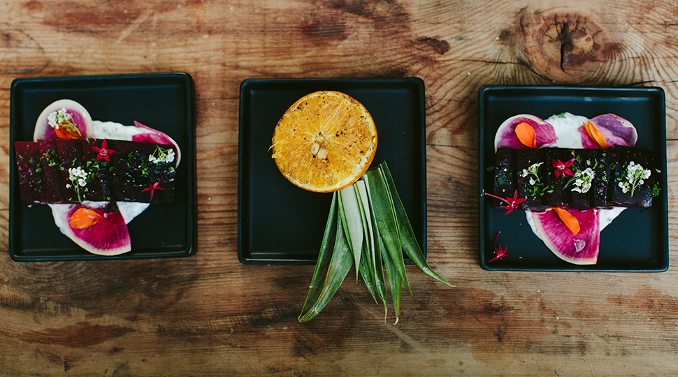 Three square black plates with colorful, floral food dishes