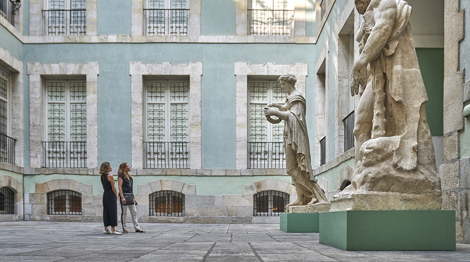 Two women in a courtyard looking up at two large marble sculptures