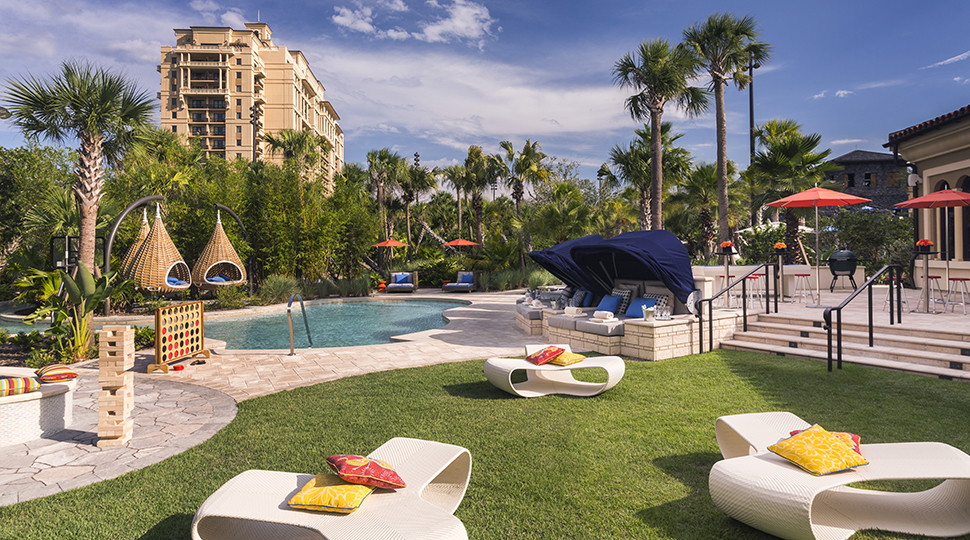 White patio chairs, hanging baskets, palm trees around swimming pool deck
