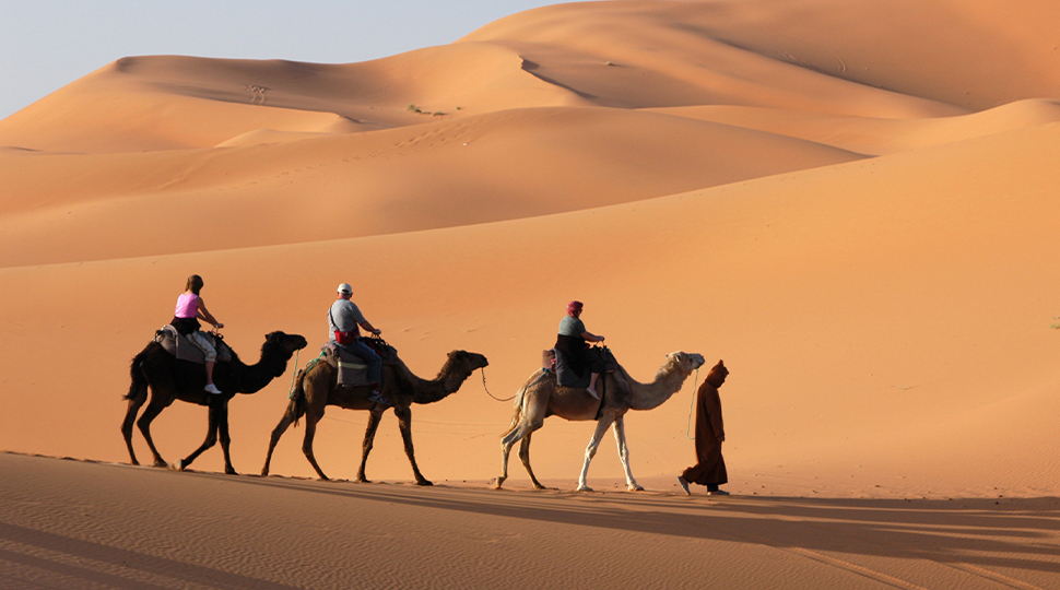 Man leads three people on camels through the Arabian Desert