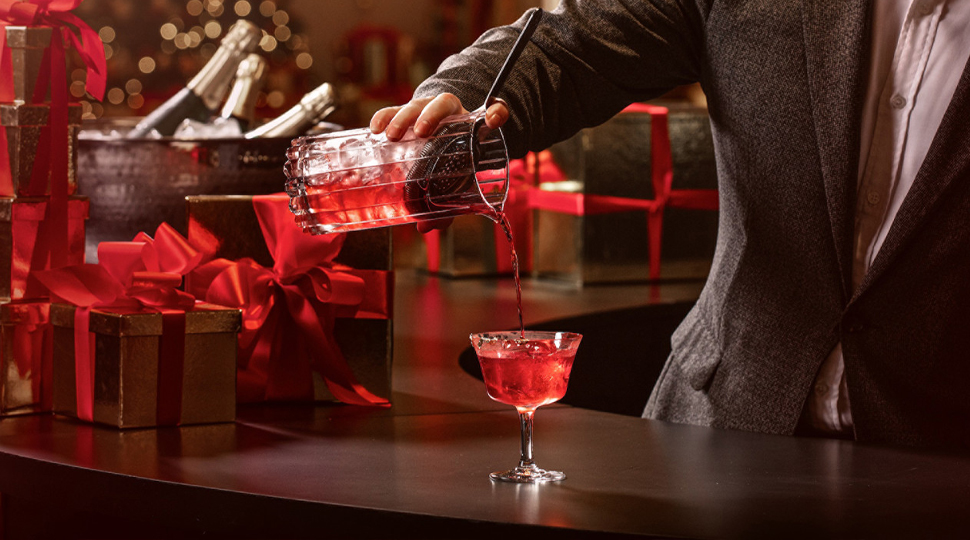A mixologist pours a red holiday cocktail