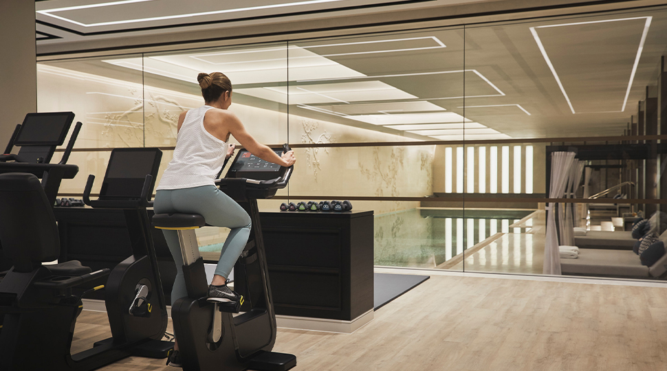 Woman riding an exercise bicycle with an indoor pool in the background