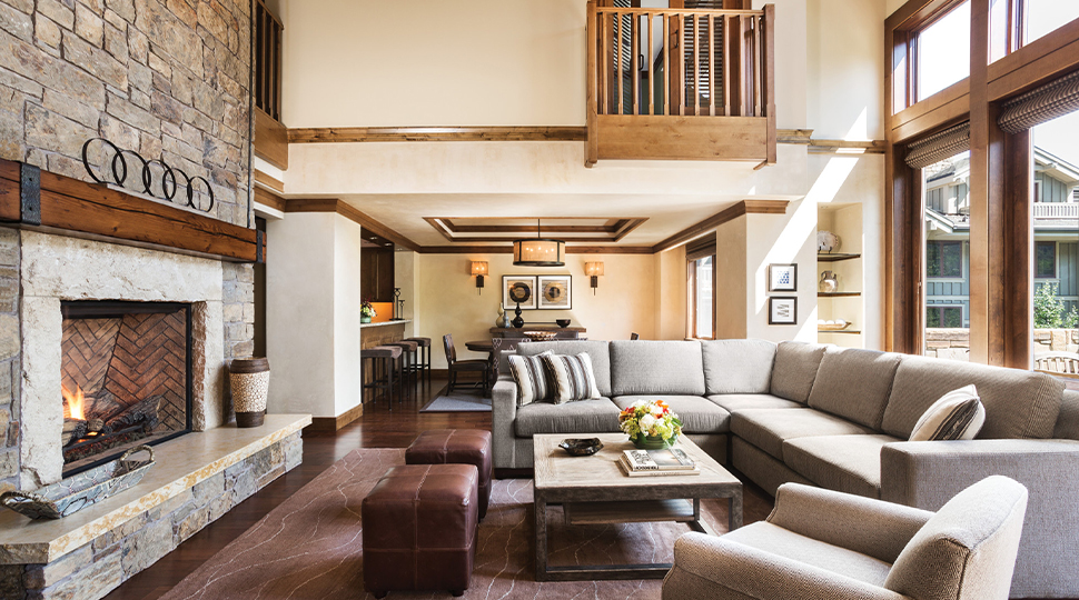 Living room with double-height ceilings, light-grey sectional couch, coffee table and large stone fireplace