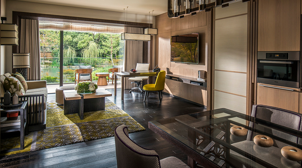 Interior view of a living room with a sitting area, dining area and television, with an open-air deck in the background