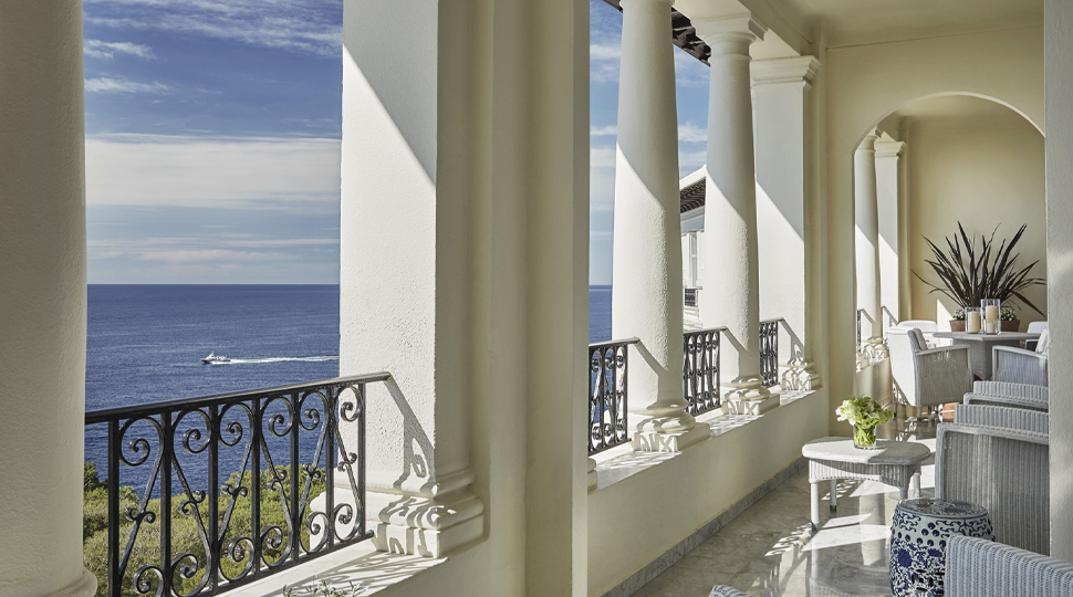 Veranda with white columns, black wrought iron details and white lounge furniture overlooking the sea