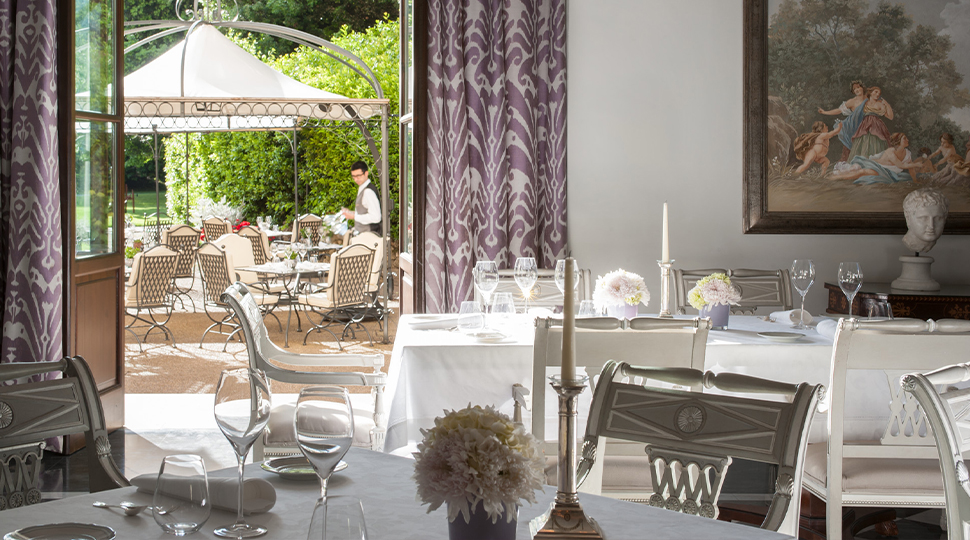 Interior of Il Palagio restaurant in Florence with white-linen tables, lavender curtains and large glass doors that open up to a garden terrace