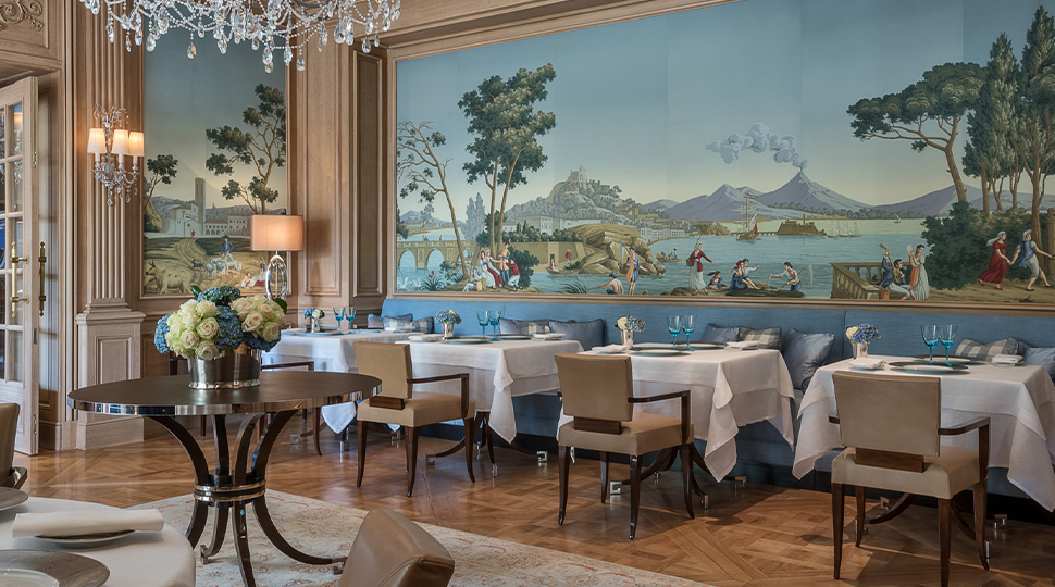 Interior of Il Lago dining room with square white-clothed dining tables set in front of a mural of Lake Geneva