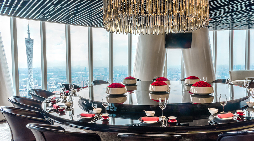 Large round dining table set for a large group at Yu Yue Heen next to floor-to-ceiling windows overlooking Guangzhou skyline