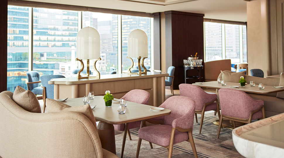 Pink upholstered dining chairs and light-wood tables and furniture fill the dining room of SÉZANNE next to floor-to-ceiling view of Tokyo