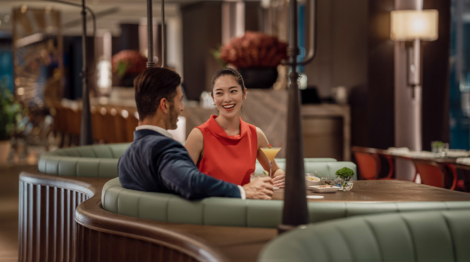 A man in a blue suit and a woman in a red dress sit at a round booth in a restaurant