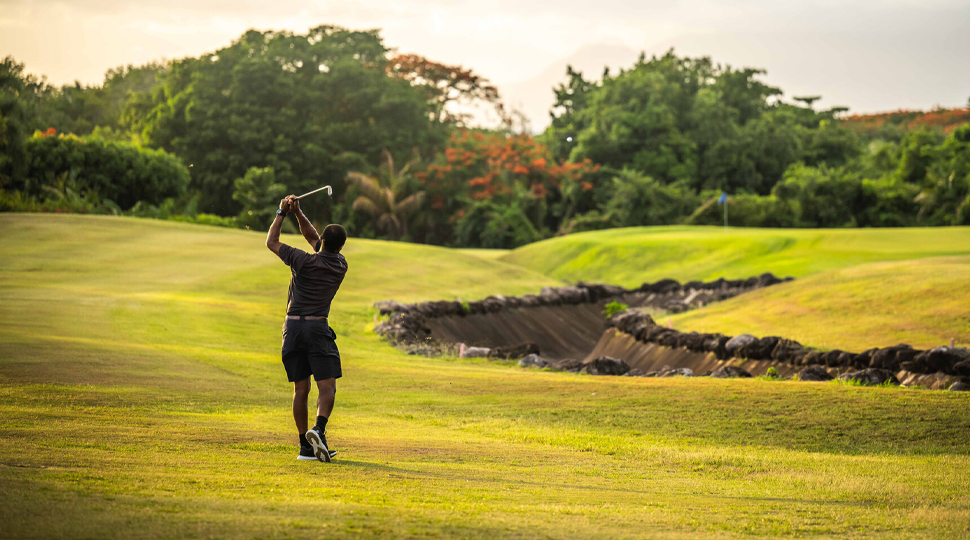 Man wearing black polo and shorts takes a swing on a golf course