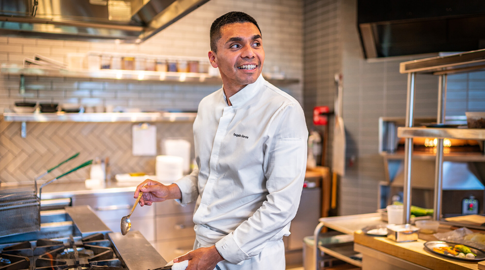 Chef Rogelio Garcia wears a white button-down shirt and stand in front of an oven in the Auro kitchen