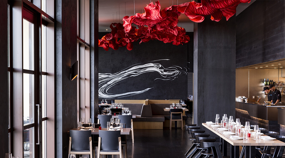 Interior of Capa dining room with black walls and a bright red art installation on the ceiling