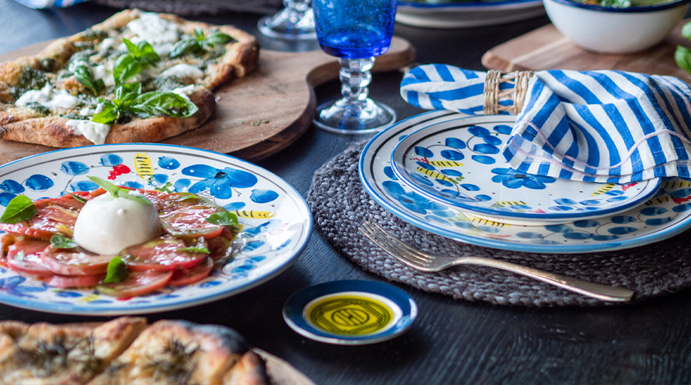 Close up of place setting featuring white-and-blue dishes, fresh sliced tomatoes, a flatbread pizza and more