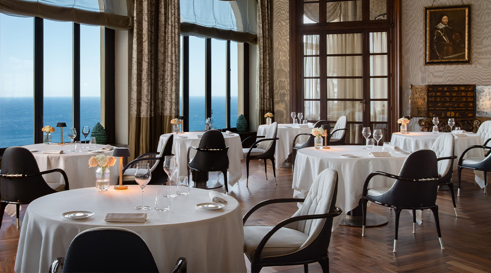 Interior of Principe Cerami dining room at San Domenico Palace in Taormina, with tables set next to large windows overlooking the ocean