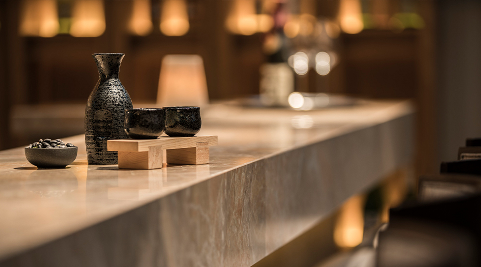 Bottle of sake and two sake cups sit on a thick marble bar counter