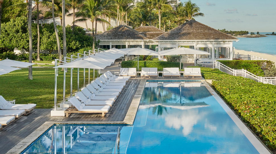 Outdoor L-shaped pol lined with white lounge chairs and a landscaped lawn