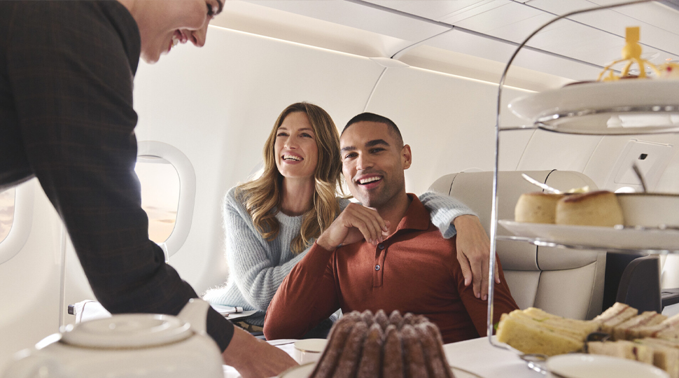 A couple sits in their seats on a private plane as a tray of sweets is brought to them by a smiling attendant