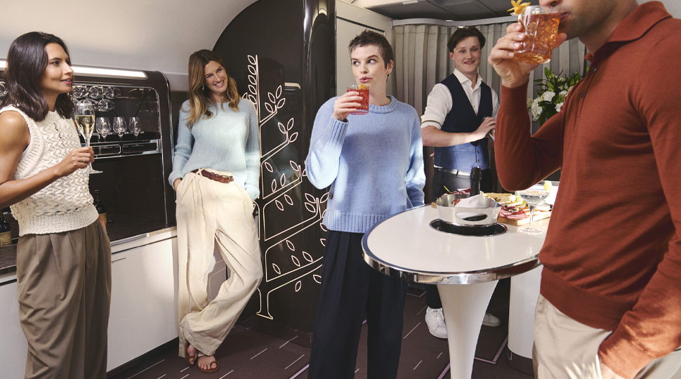 Five people stand in a lounge area board a private plane, with three sipping drinks