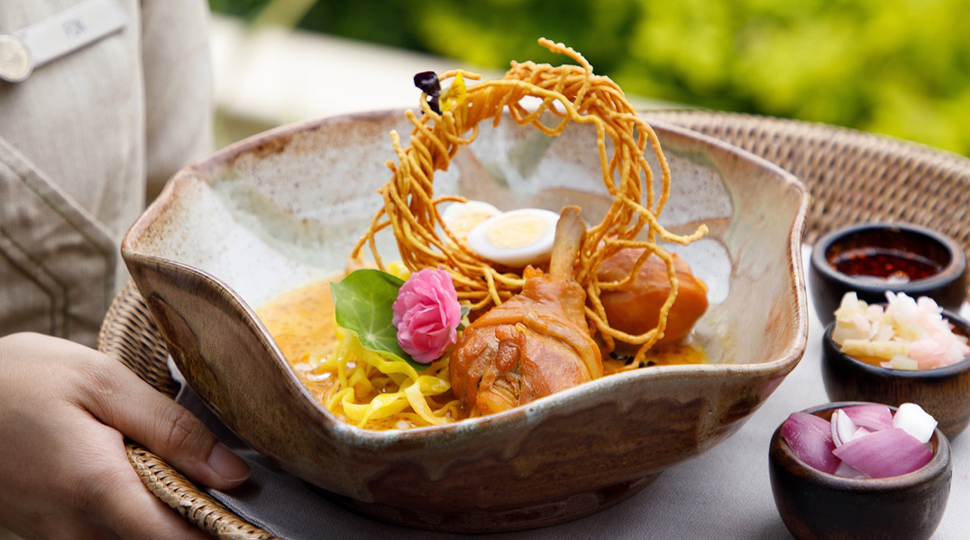 Khao soi gai dish with noodles, two chicken drumsticks and a wreath of crispy noodles served in an organic-edged bowl