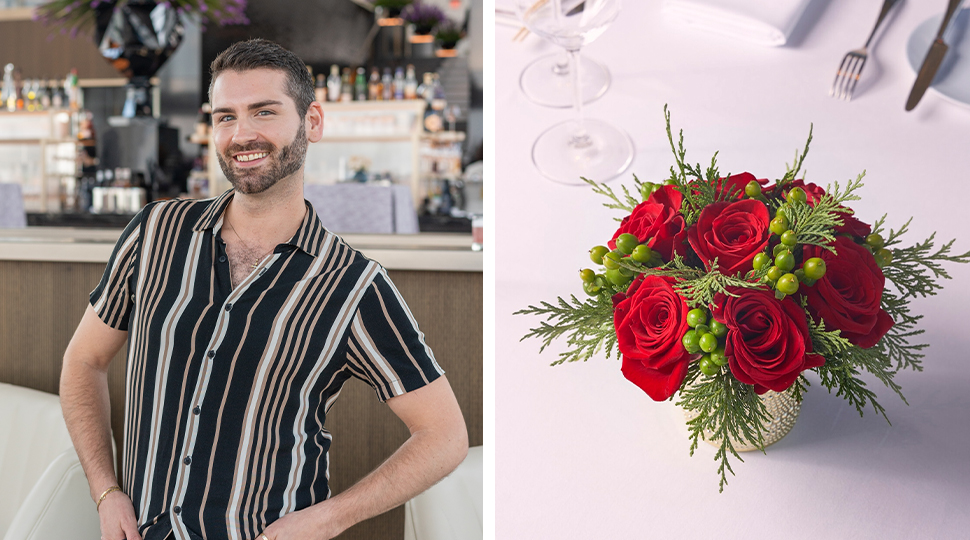 Person with short dark hair and a short beard stands with arms akimbo wearing a button down shirt with black, grey and white vertical lines; Right: Small bouquet of red roses and green berries and leaves sits atop a white table