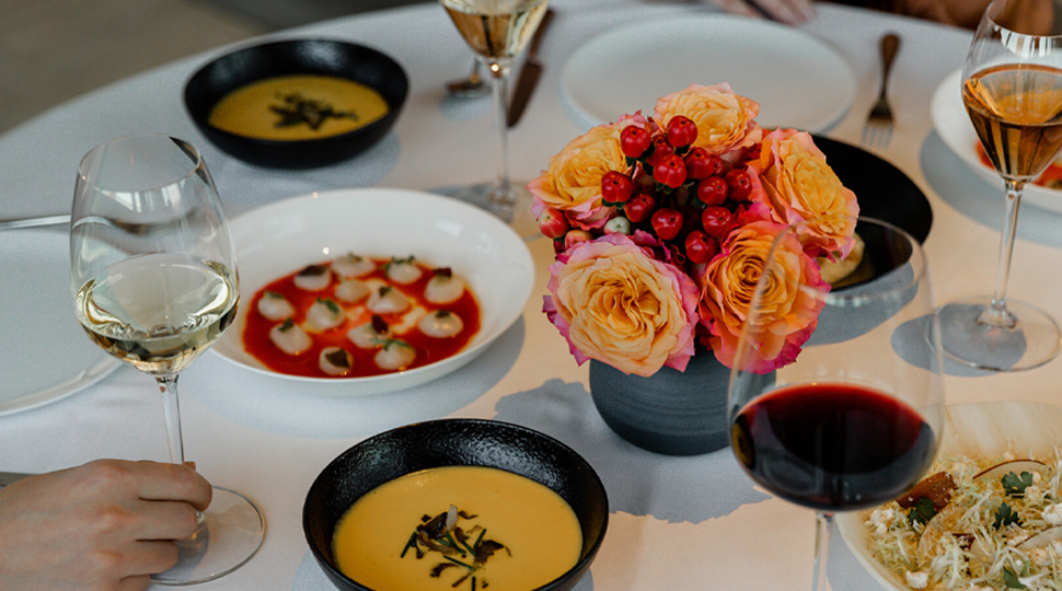 Dining table filled with various soups in red and orange colours with a bouquet of light-orange blooms and red ilex berries