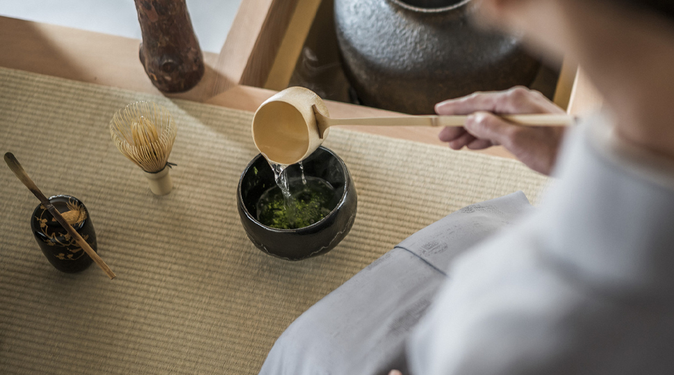 Person's hand pours tea into a small black cup
