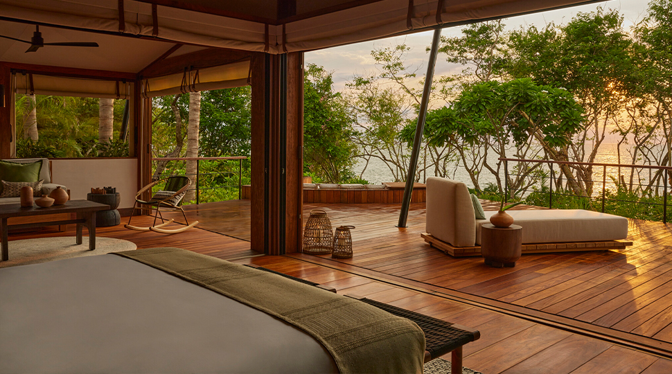 Indoor-outdoor bedroom opens up to a large wooden deck overlooking the jungle