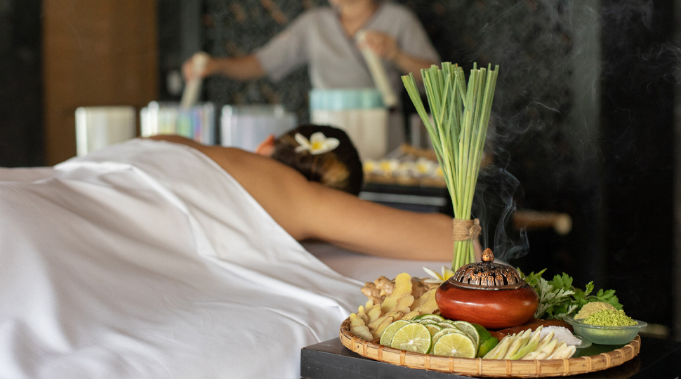 Platter of sliced ginger, lime, apples and other fresh produce sits next to a guest getting a massage