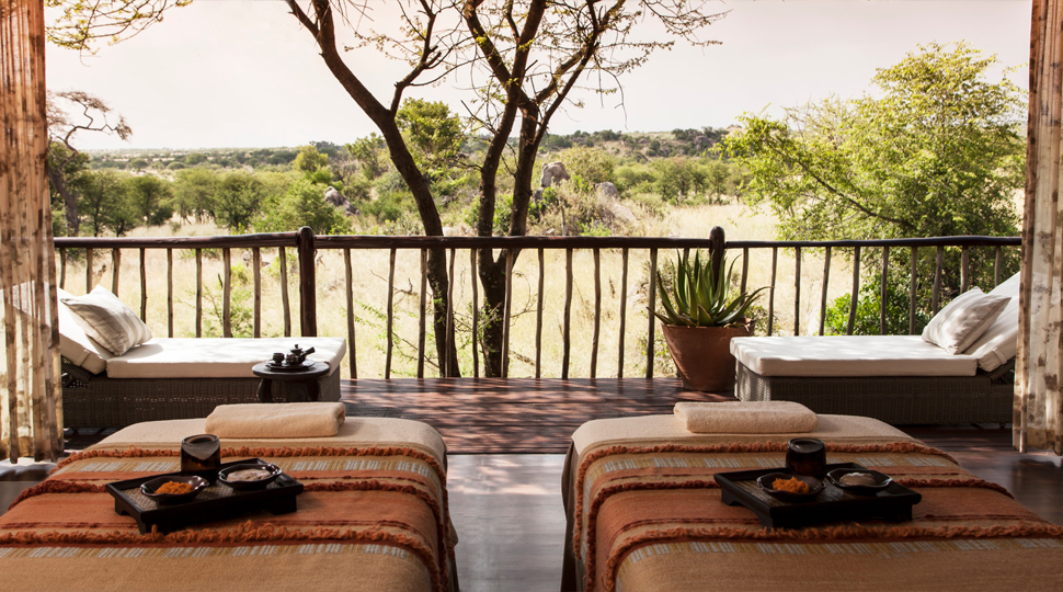 A spa treatment room with two massage tables opens up to a deck with two lounge chairs