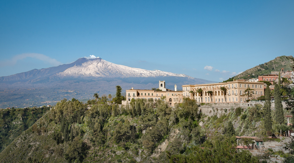 Hotel set on a rocky hillside with a snow-capped mountain in the disntance