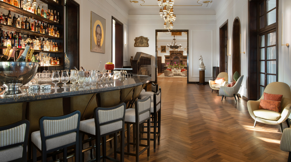 Curved bar with a tall shelf behind it, wooden parquet floors and arm chairs in a hotel bar